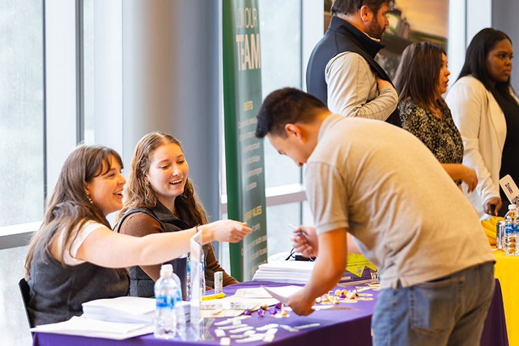 Students from a Registered Student Organization sit at a table in at the RSO fair speaking with a student who is signing up to join.