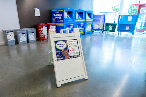 A sign that says Donate Here in front of a row of donation bins.