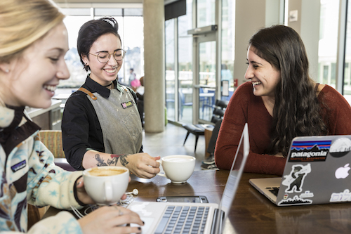 A barista gives a coffee mug to a smiling student