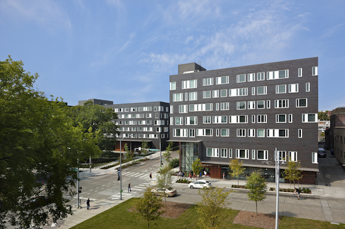 A street filled with cars in front of gray buildings.