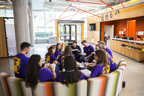 Students in matching purple shirts meet in a circle in Area 01