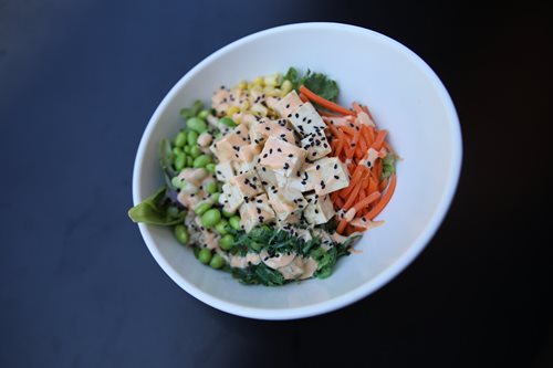 Bowl of tofu and colorful veggies with black sesame seeds and orange citrus dressing.